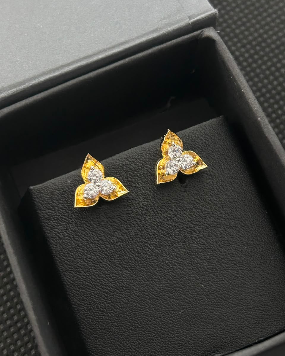 A pair of gold butterfly stud earrings with clear gemstones, displayed on a black velvet jewelry box insert inside an open black box.