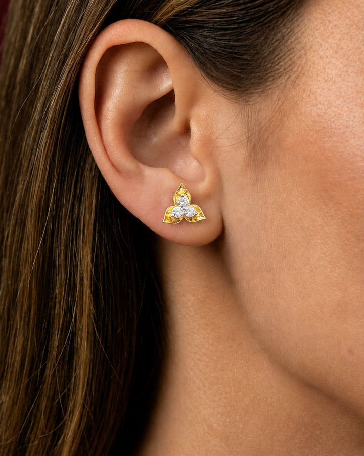 A close-up of a woman's ear wearing a small gold stud earring with three clear gemstones in a triangular arrangement.