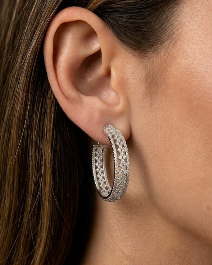 A close-up of a model's ear wearing a silver hoop earring adorned with pavé-set clear stones.