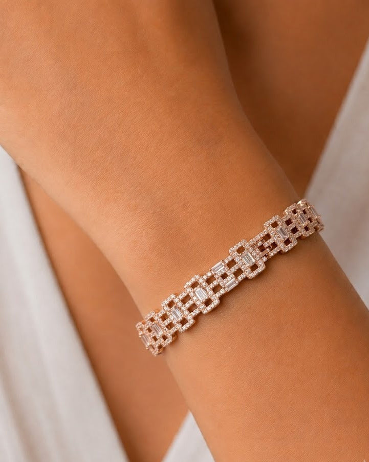 A close-up of a rose gold link bracelet with clear baguette and round-cut stones worn on a person's wrist, set against a soft white top.