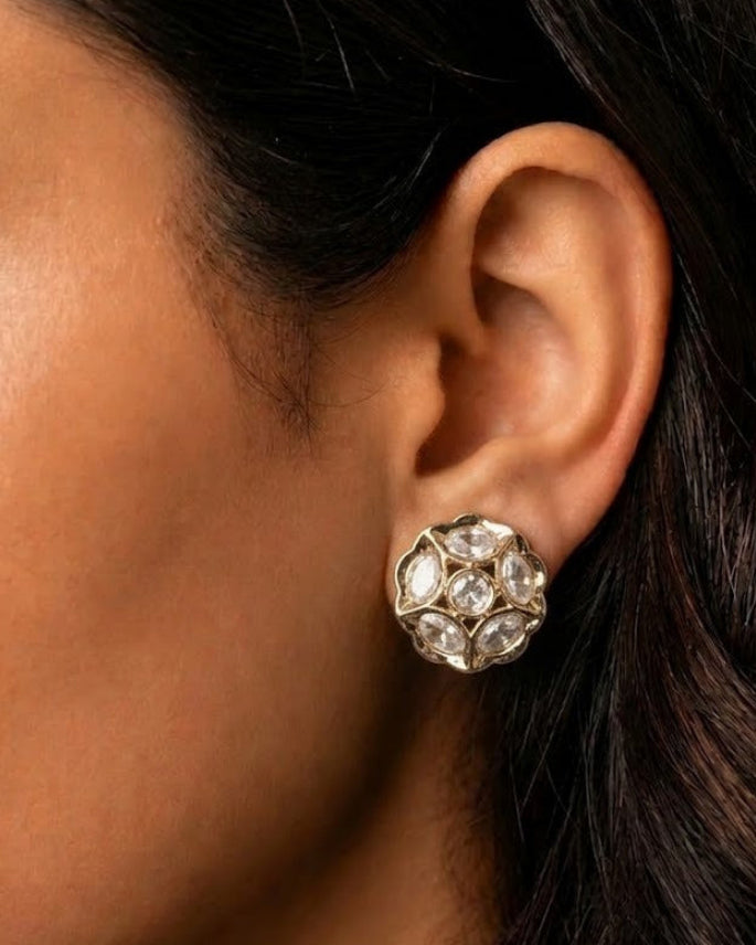 A close-up of a person's ear wearing a gold-toned cluster stud earring with clear gemstones.