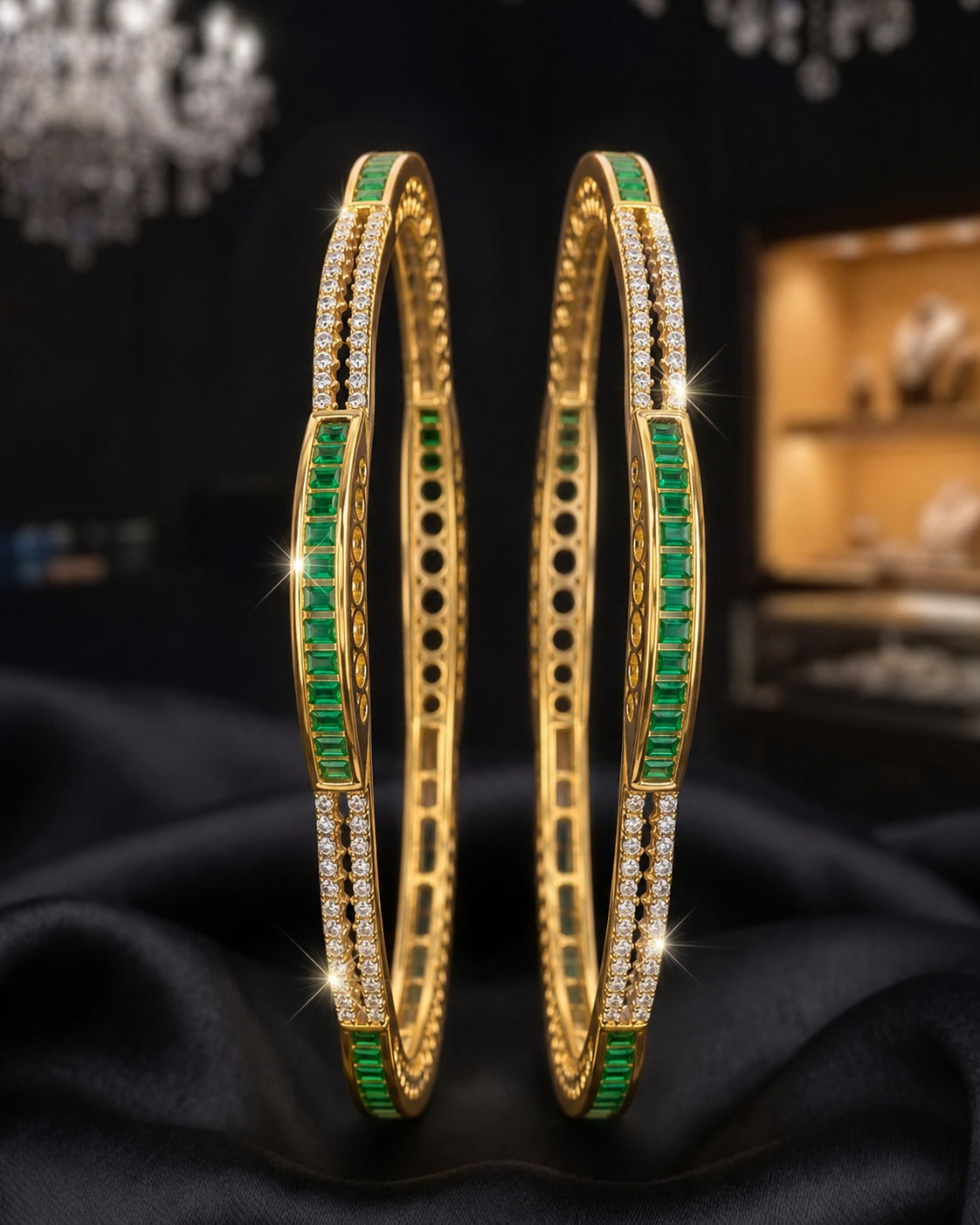 Two gold bangles with green and clear stone detailing, displayed on a black satin surface with a blurred luxury jewelry store background.