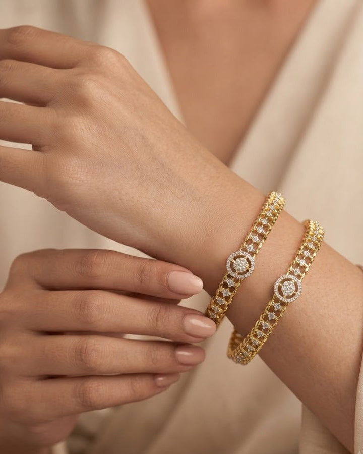 Two gold-toned diamond-embellished bracelets worn on a model's wrist, shown against a soft beige robe.