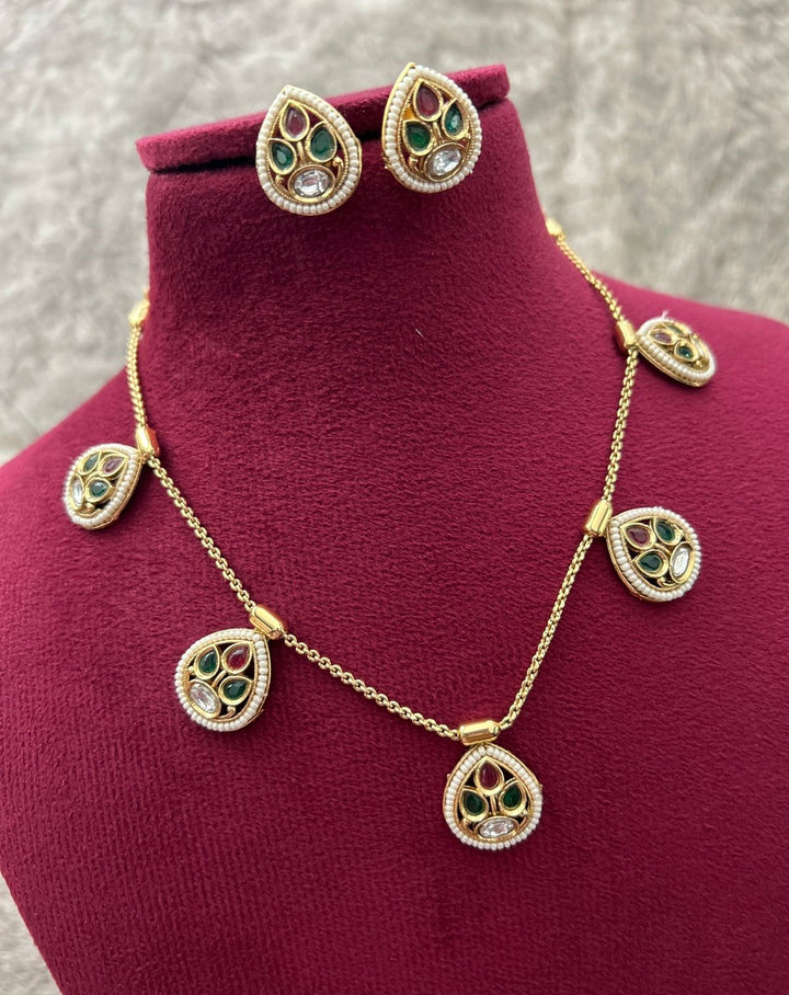 Gold necklace and earrings with green and red stones on a mannequin bust.