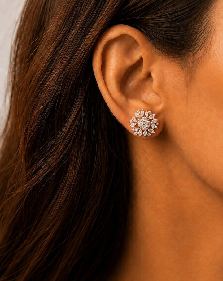 A close-up of a woman's ear wearing a small floral stud earring with clear stones in a silver-toned setting.