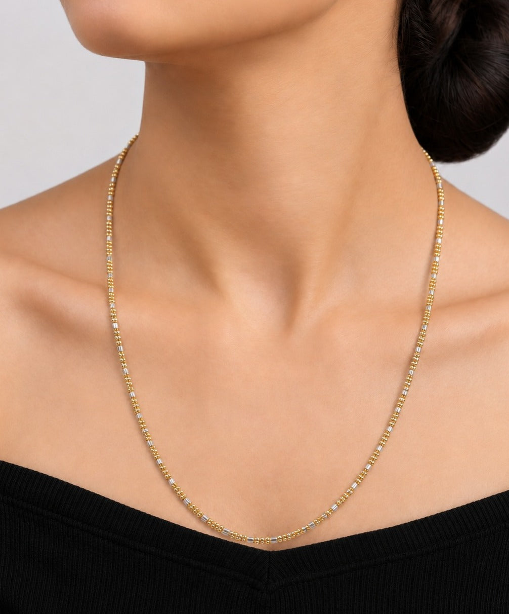A close-up of a model's neck and upper chest wearing a delicate gold tennis-style chain necklace with small clear stones, paired with a black off-the-shoulder top.