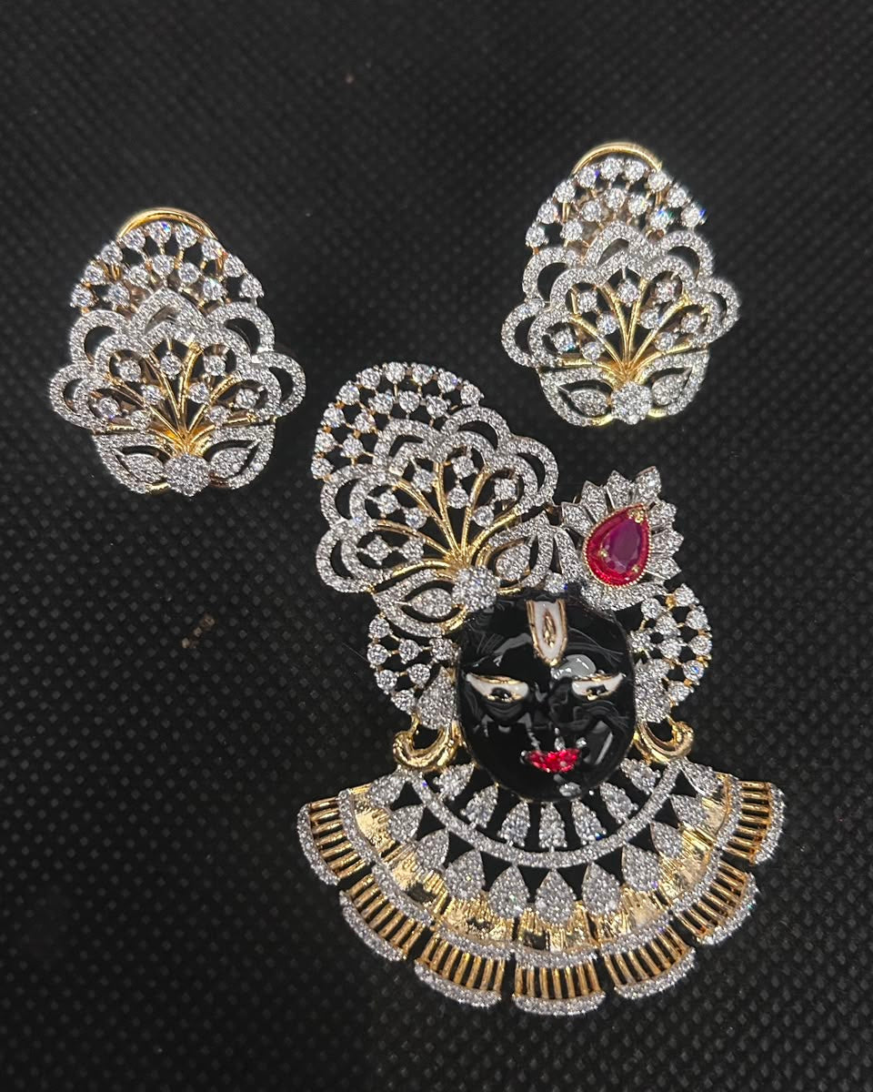A gold and silver-toned jewelry set featuring a large decorative brooch with a black face, red gemstone, and intricate pavé detailing, accompanied by two matching fan-shaped earrings, displayed on a black textured background.