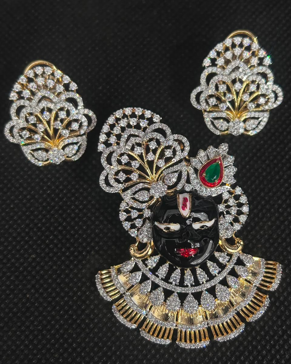 A gold and silver jewelry set featuring a central decorative piece with a black face, red and green gemstone accents, and a scalloped silver-and-gold pattern, shown with two matching silver-and-gold leaf-shaped pieces on a black textured background.
