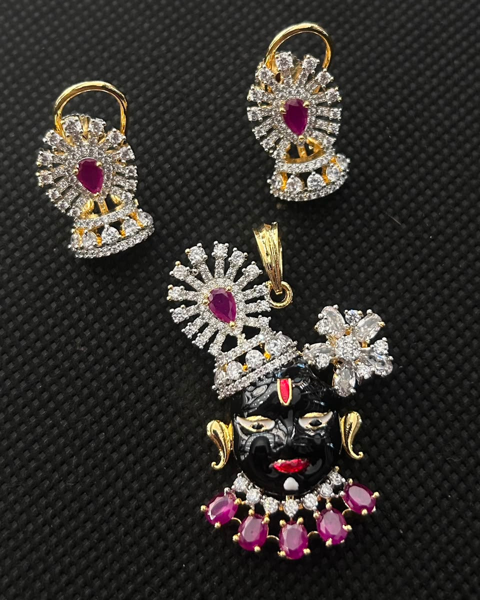Gold and silver jewelry set featuring a Lord Krishna pendant and matching earrings, embellished with clear crystals and pink gemstones, displayed on a black textured background.