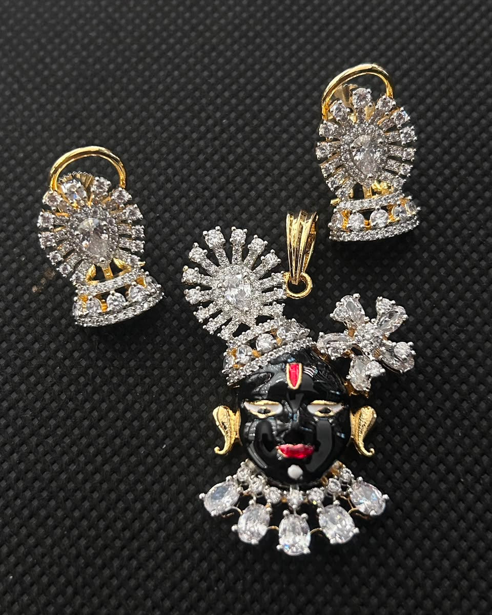 A jewelry set featuring a black and gold Lord Krishna pendant with clear rhinestones, accompanied by two matching gold and silver earrings with clear rhinestones, displayed on a black textured background.