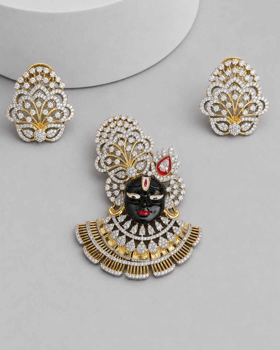 Gold and silver-tone jewelry set featuring a central decorative piece with a black face motif, red accents, and a scalloped crystal-encrusted design, shown with two matching crystal-and-gold leaf-shaped earrings on a light gray background.