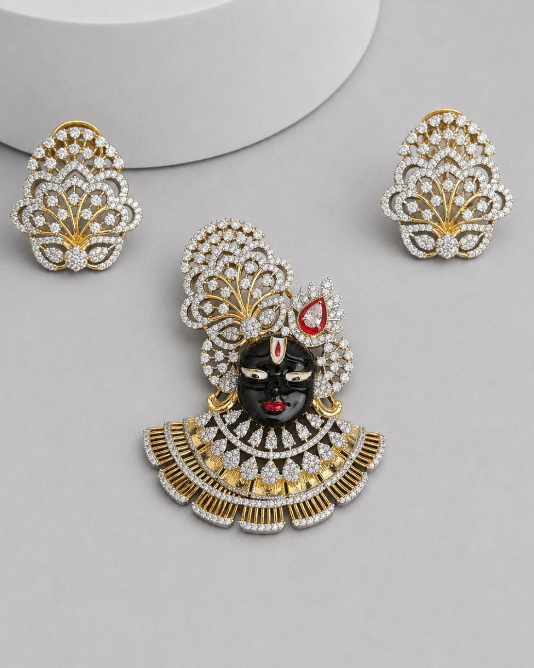 Gold and silver-tone jewelry set featuring a central decorative piece with a black face motif, red accents, and a scalloped crystal-encrusted design, shown with two matching crystal-and-gold leaf-shaped earrings on a light gray background.