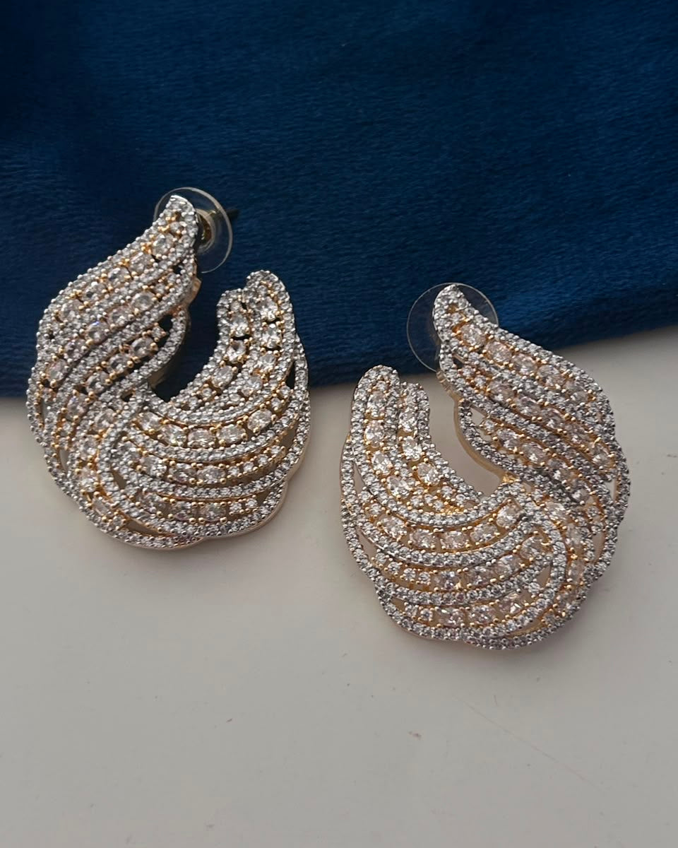 A pair of silver-toned crescent-shaped hoop earrings heavily embellished with clear rhinestones, displayed on a light surface with a dark blue velvet background.