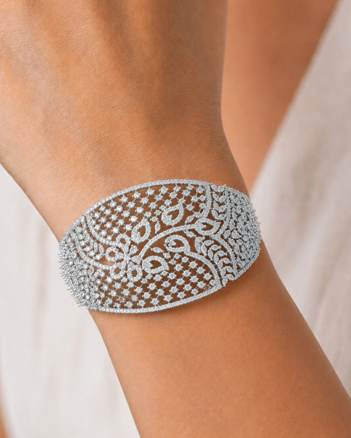 A close-up of a delicate silver-toned cuff bracelet adorned with intricate floral filigree and small clear stones, worn on a person's wrist.