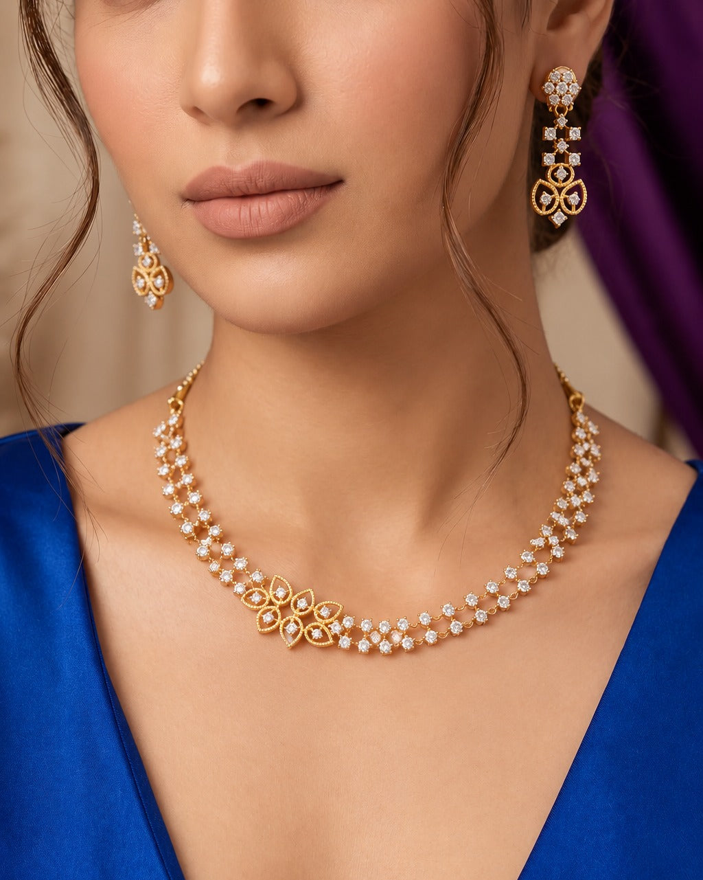 A close-up of a model wearing a gold and pearl necklace with matching drop earrings, styled with a royal blue satin top.