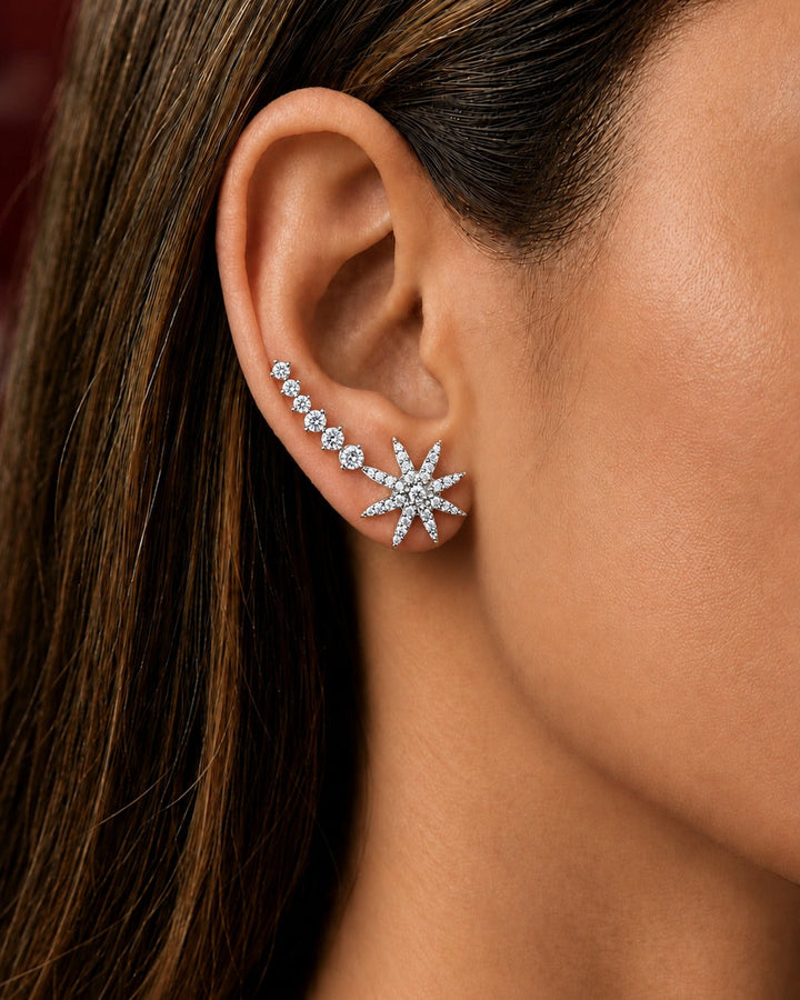 A close-up of a model's ear wearing a silver-toned starburst stud earring and a matching curved ear cuff with small clear stones.