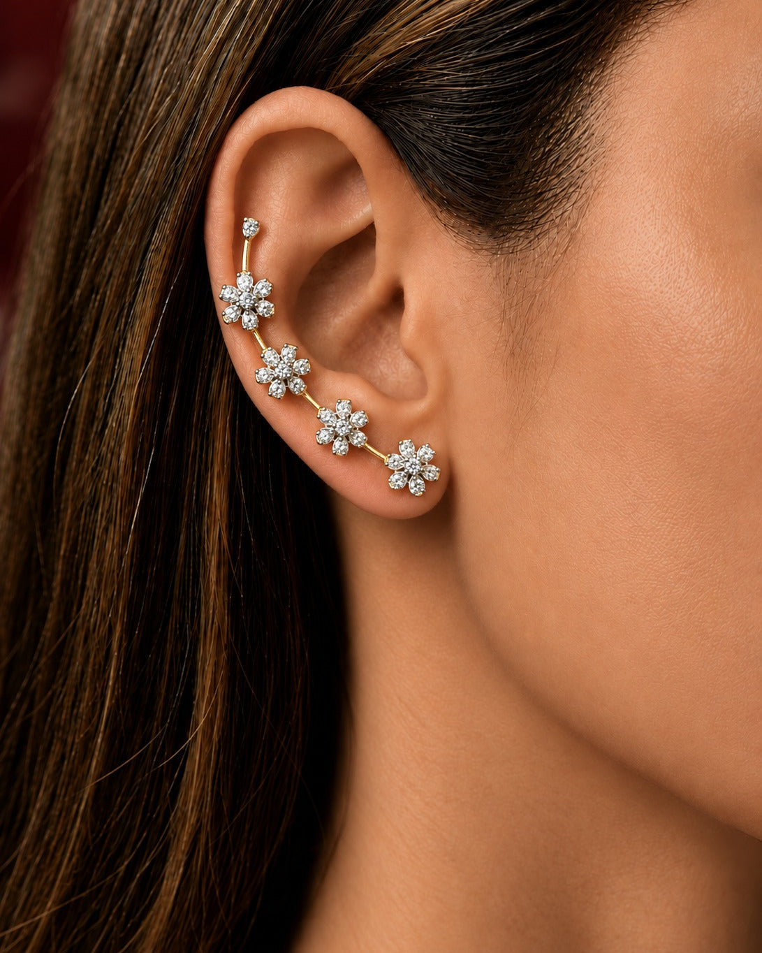 A close-up of a woman's ear wearing a gold ear cuff adorned with four snowflake-shaped clusters of clear stones.