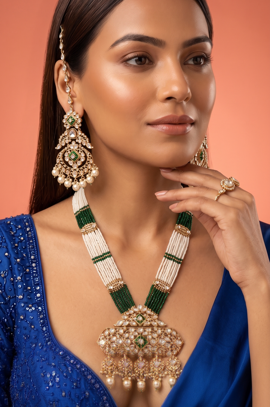 Woman wearing a blue outfit with a long, ornate necklace and matching earrings against an orange background
