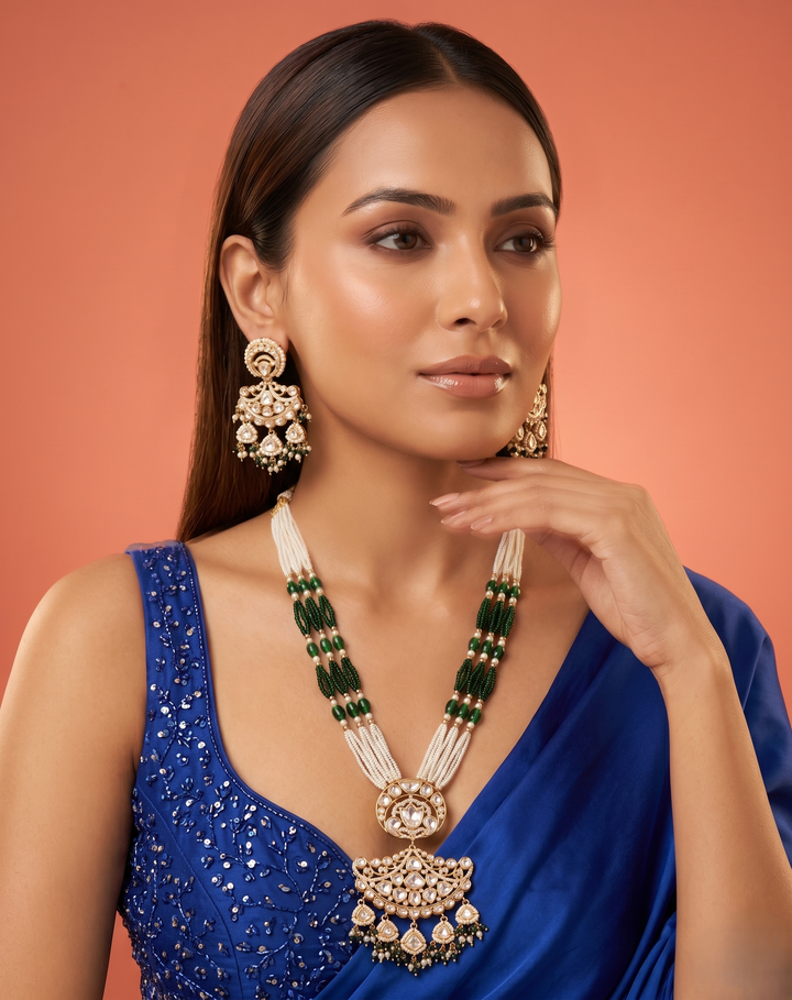 Woman wearing a blue saree with gold and green jewelry against an orange background
