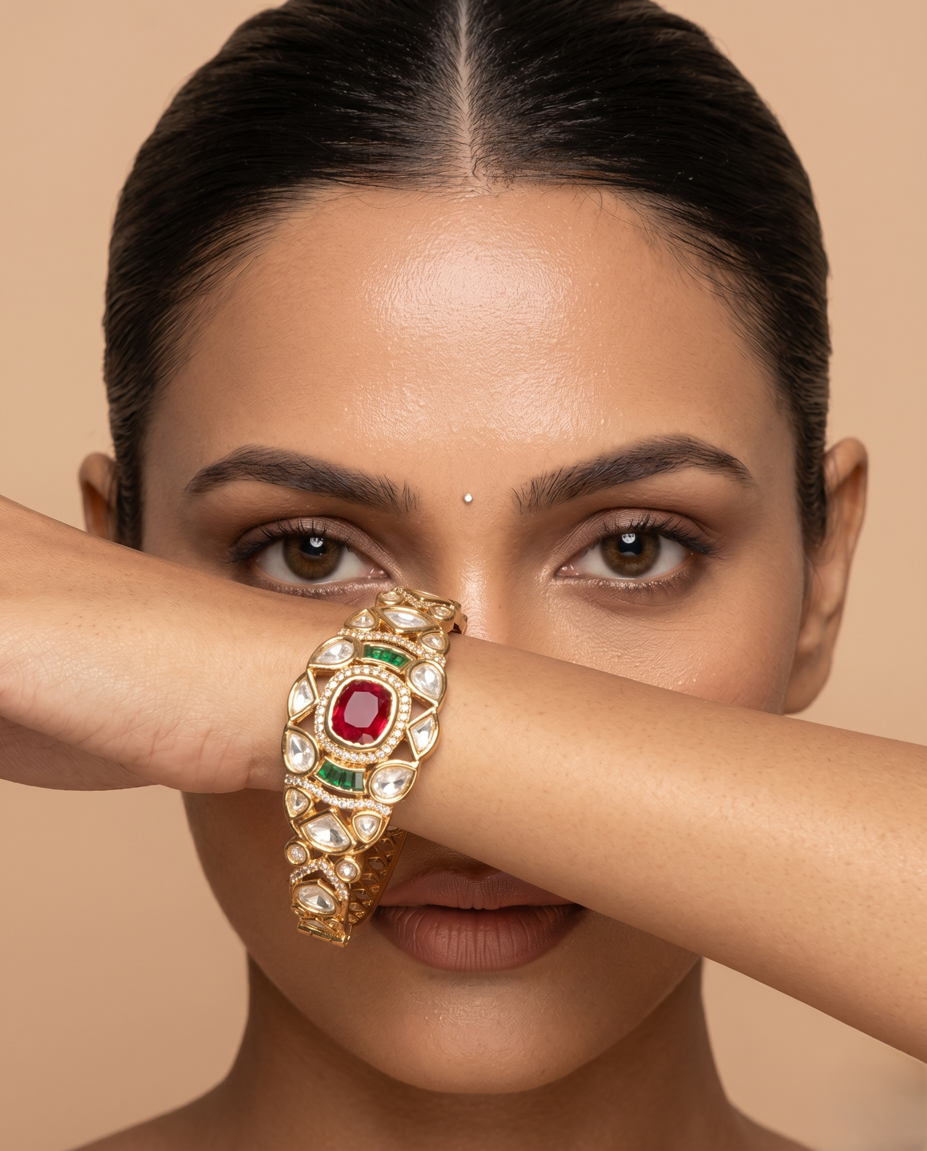 Woman wearing a gold bracelet with a red gemstone against a beige background