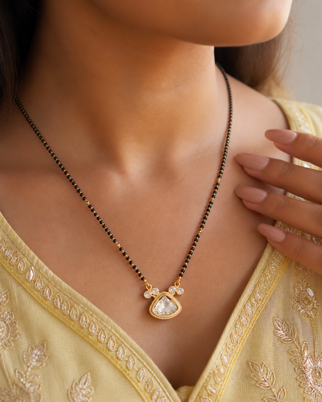 Woman wearing a gold necklace with a pendant, dressed in a yellow saree.