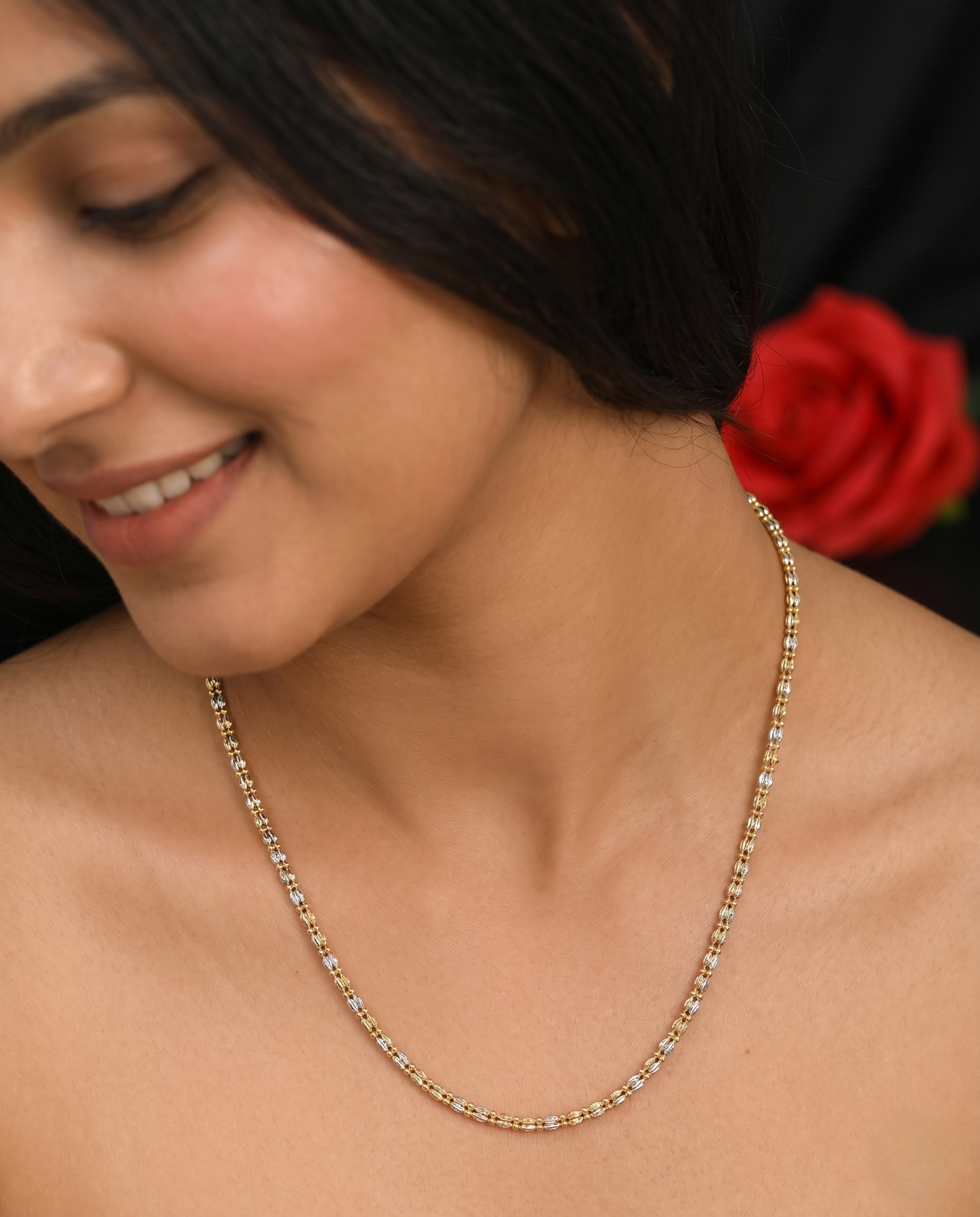 Woman wearing a gold necklace with a red rose in the background