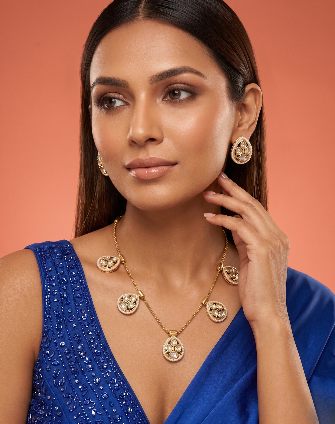 Woman wearing gold jewelry set against a warm-toned background