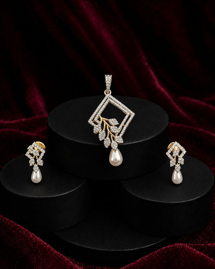 A jewelry set featuring a diamond-shaped pendant with a dangling pearl and leaf motif, paired with matching drop earrings, displayed on black cylindrical pedestals against a dark red velvet background.
