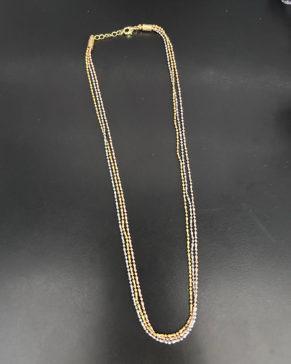A delicate two-strand necklace with alternating gold and silver-toned links, laid flat on a dark gray surface.