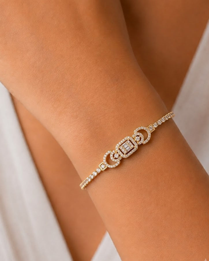 A delicate gold bracelet with pavé-set clear stones, featuring a central square motif and curved side details, shown worn on a person's wrist.