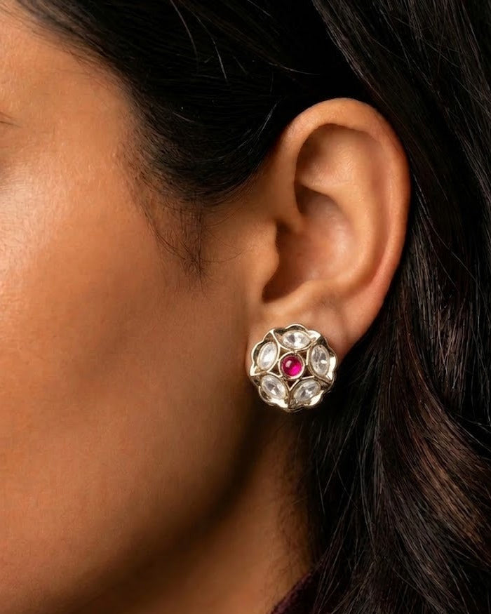 A close-up of a woman's ear wearing a silver-toned flower-shaped stud earring with a central pink gemstone and clear stones around it.