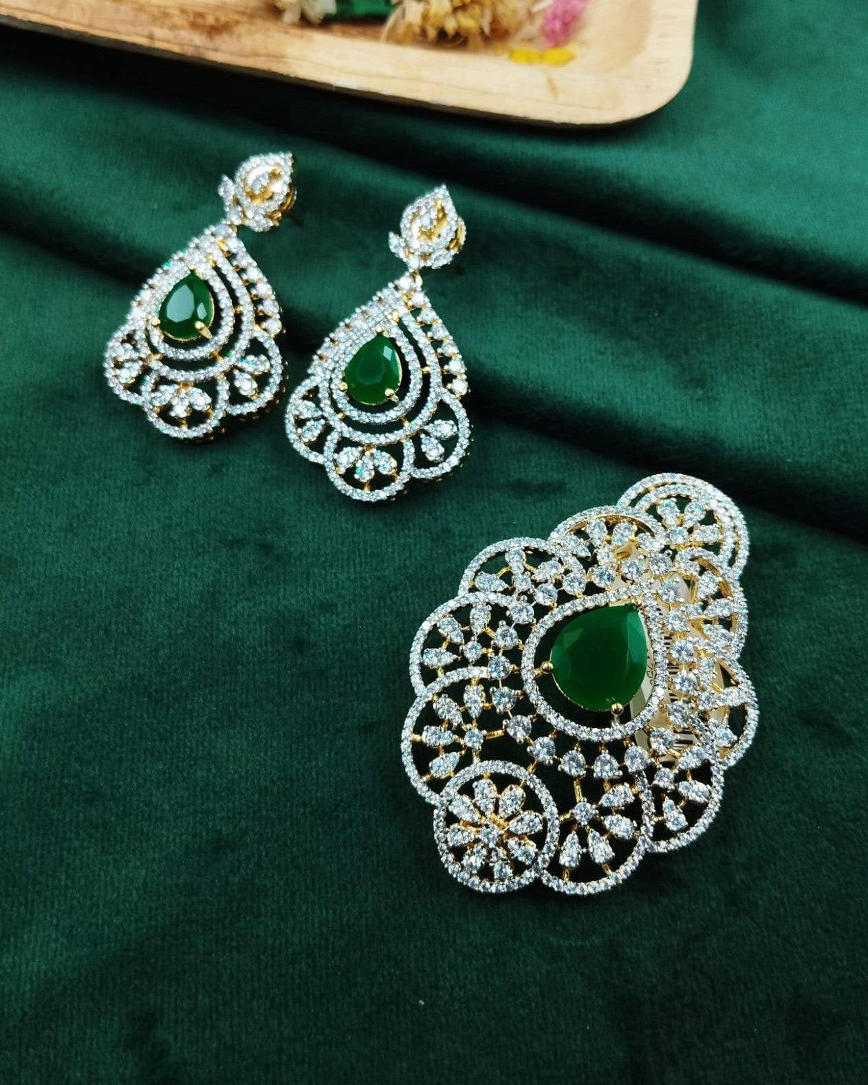 Ornate earrings with green gemstones on a dark green fabric background