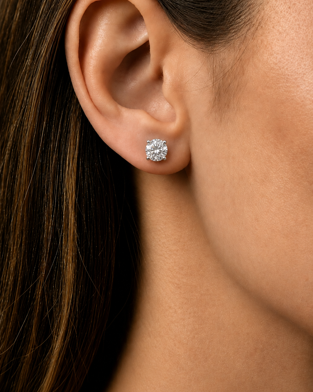 A close-up of a woman's ear wearing a small round brilliant-cut diamond stud earring.