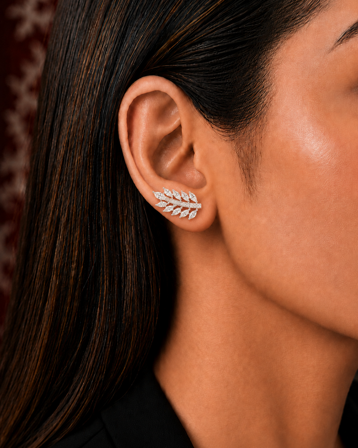 A close-up of a woman's ear wearing a delicate leaf-shaped stud earring set with small clear stones in a silver-toned metal.