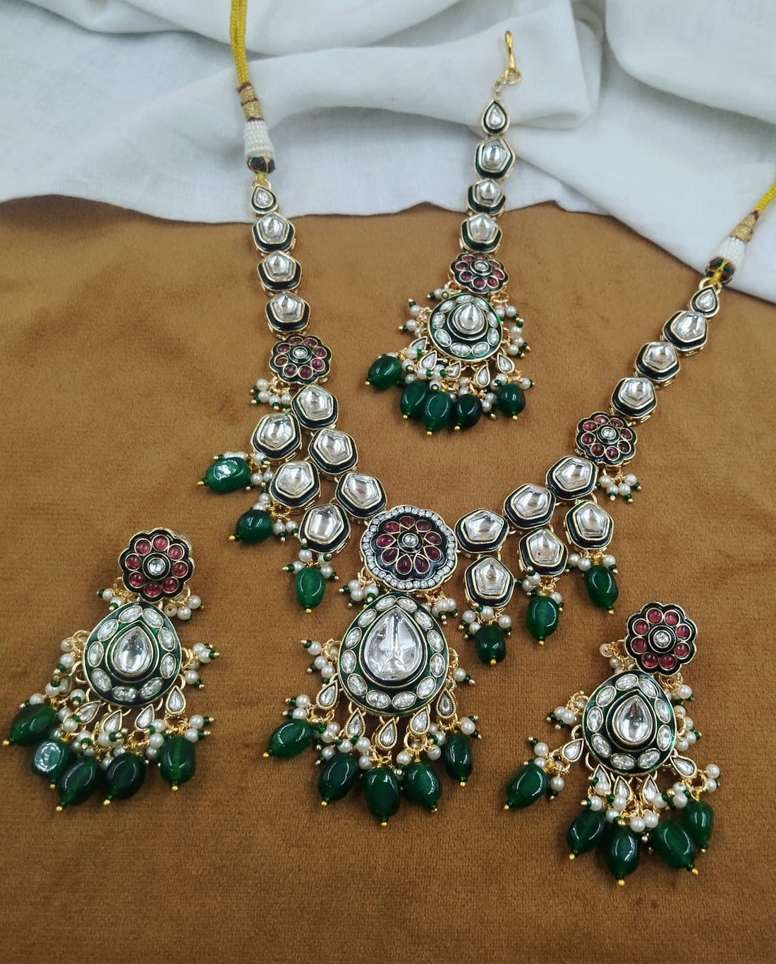 Close up view of green kundan pearl necklace set with earrings and maang tikka in gold finish