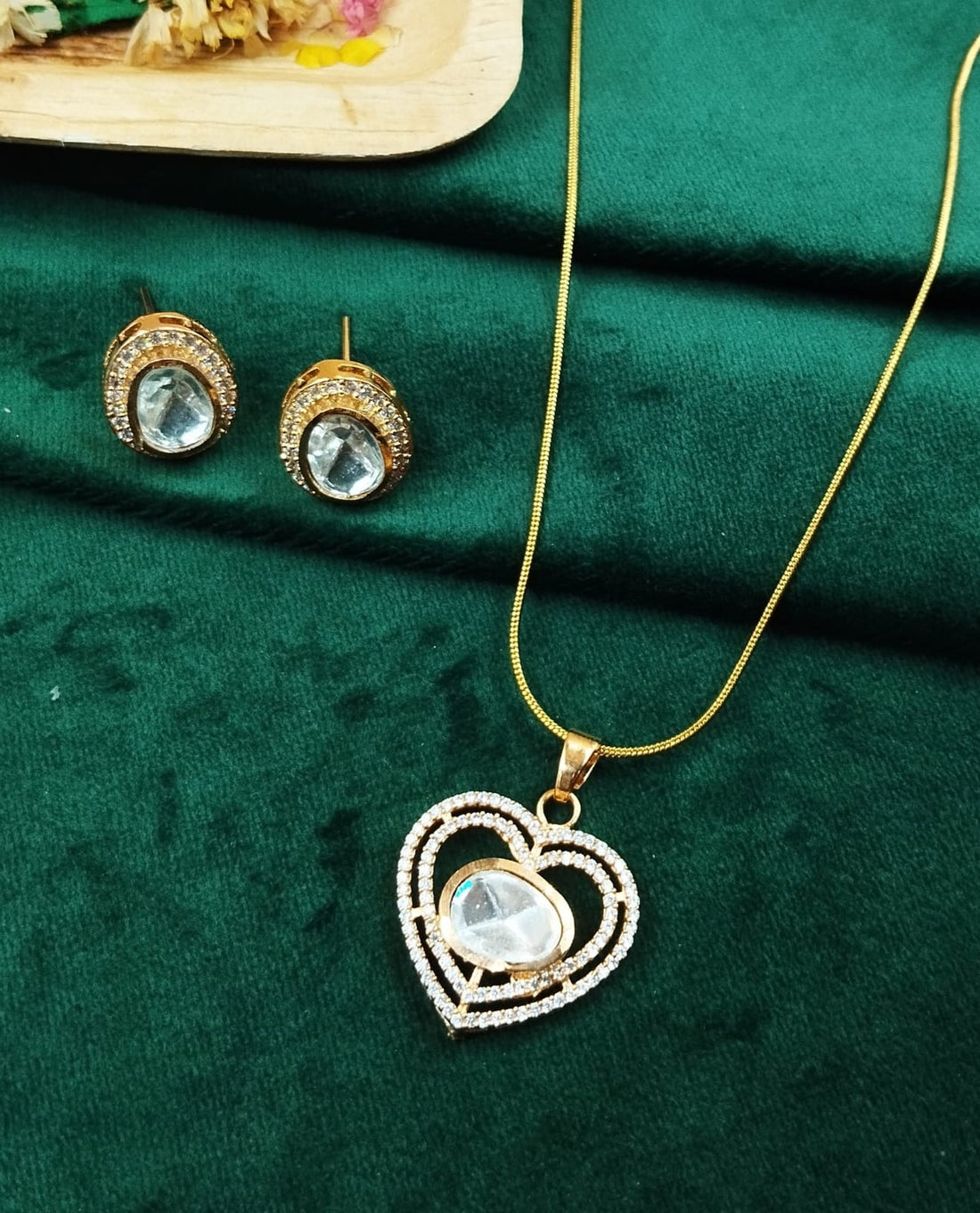 Gold necklace with heart-shaped pendant and matching earrings on a green fabric background