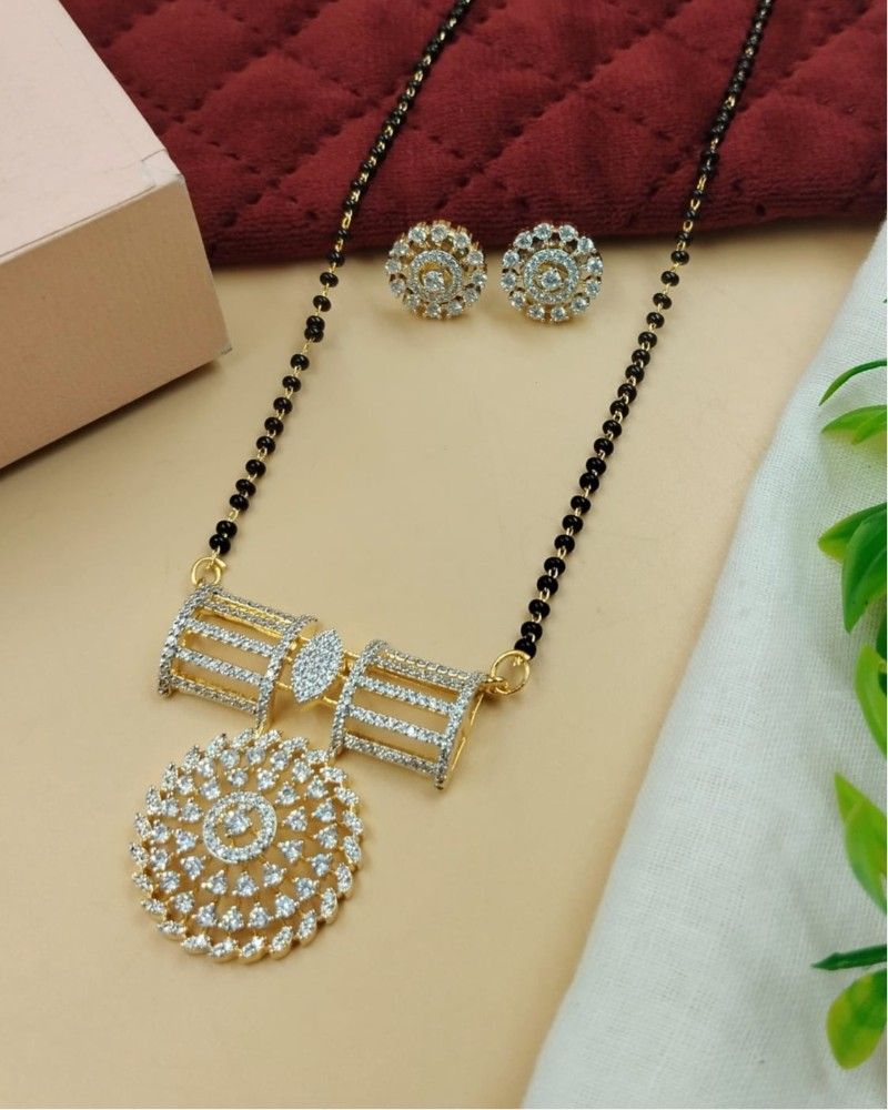 Gold necklace with black beads and matching earrings on a beige surface.