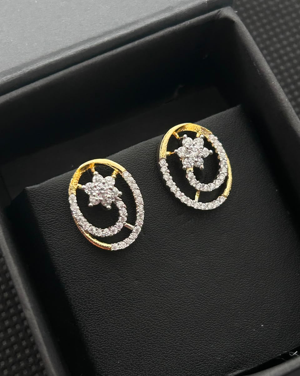 A pair of gold and silver-tone stud earrings with a crescent moon and star design, set with clear pavé stones, displayed inside a black jewelry box.