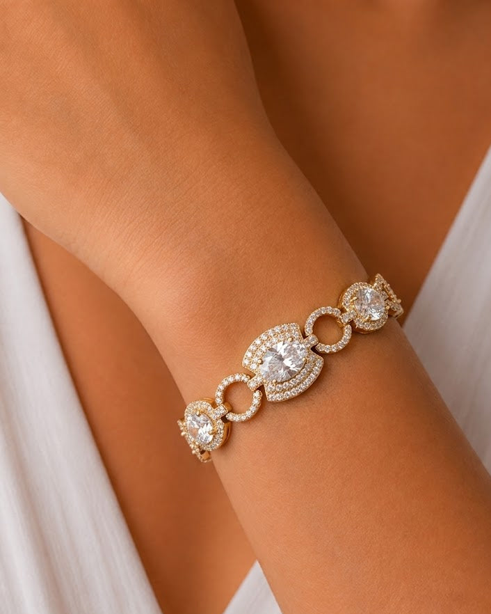 A close-up of a gold-toned bracelet with clear gemstones and pavé detailing, worn on a person's wrist.